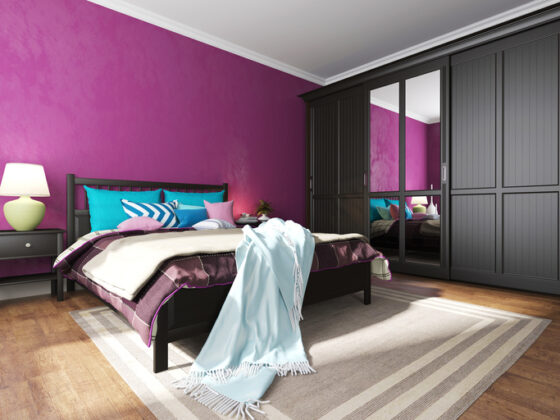 Hotel bedroom interior with black furniture, a rug and pillows on a bed and a wardrobe with a mirror on the floor with carpet